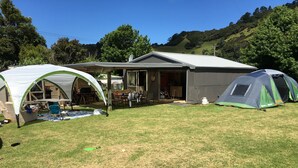 Zona de camping con una tienda de campaña, un pequeño edificio con porche y un campo cubierto de césped.