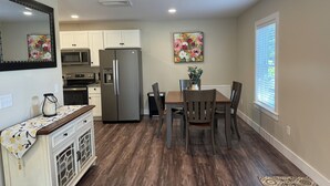 A modern kitchen with white cabinets, stainless steel appliances, and a dining area with wooden chairs and a table.
