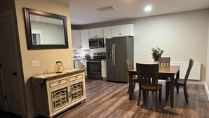 A modern kitchen with white cabinets, a dark refrigerator, and a dining area with wooden chairs and a table.