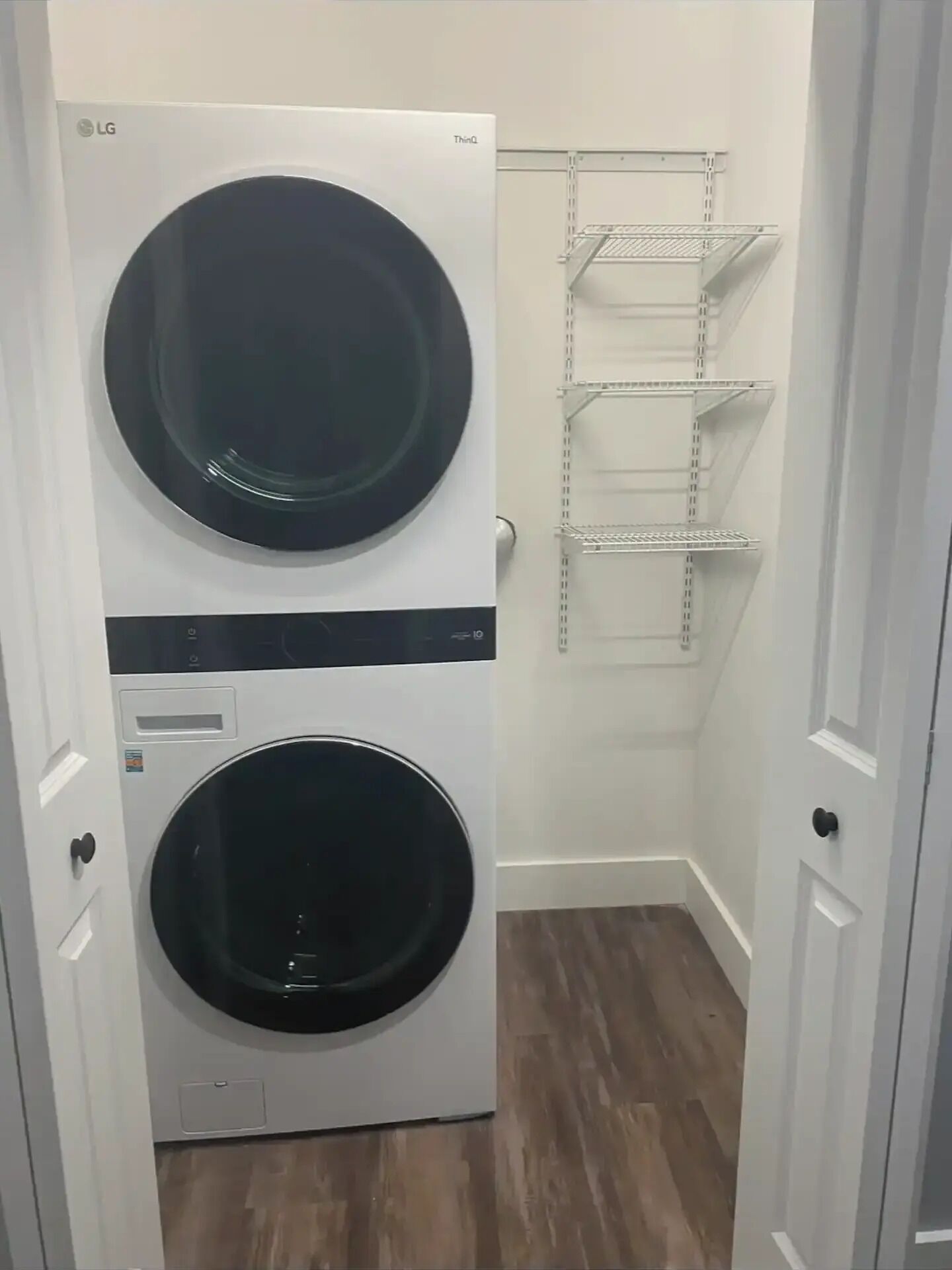 Une buanderie équipée de deux machines à laver LG superposées et d’une étagère métallique.