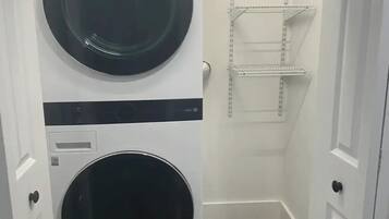 Une buanderie équipée de deux machines à laver LG superposées et d’une étagère métallique.