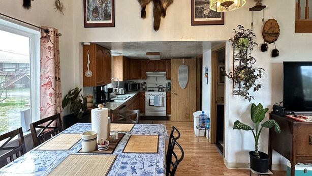 A dining area with a table set for four, wooden flooring, and a kitchen in the background.