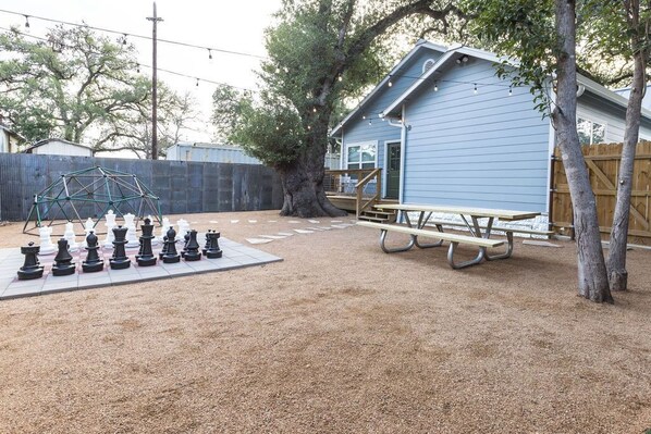 Un jardin avec un jeu d’échecs, une table de pique-nique et un abri de jardin bleu.