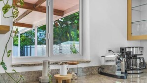 Una cocina con cafetera, hervidor y un taburete de madera.