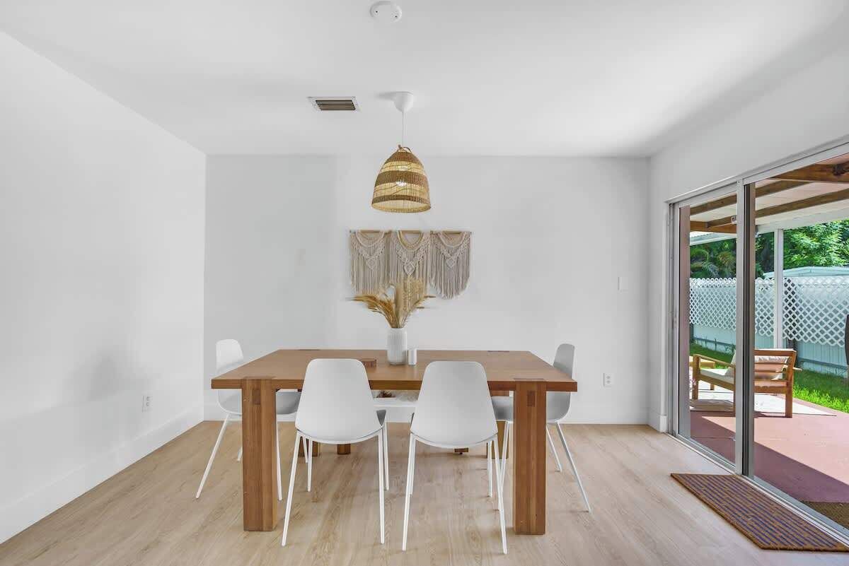 Un'area pranzo moderna con un tavolo in legno e sedie bianche, un lampadario a sospensione e vista sull'esterno tramite una porta vetrata.