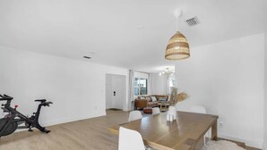 Un espacio habitable moderno con una mesa de comedor de madera, sillas blancas, un sofá y un ventanal grande.