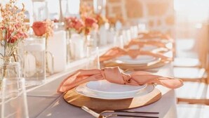 Una larga mesa de comedor vestida con manteles blancos, platos con borde dorado y cristalería transparente.