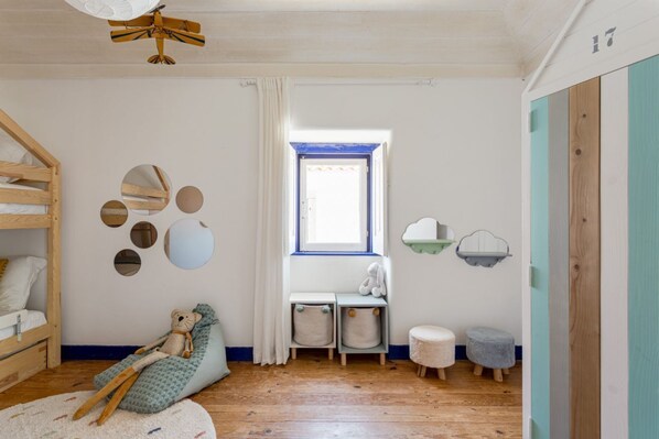 A child's room with a bunk bed, a bean bag chair, a window with curtains, and a small desk with a chair.