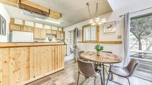 A modern kitchen with wooden cabinets, a dining area with a round table and chairs, and a large window with a view of trees. - Relaxing Ruidoso Retreat: Walk to Midtown! (Ruidoso)