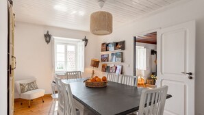 A dining area with a long table, white chairs, a basket of oranges, and a hanging light fixture. - Exceptional house near Colares (Colares)
