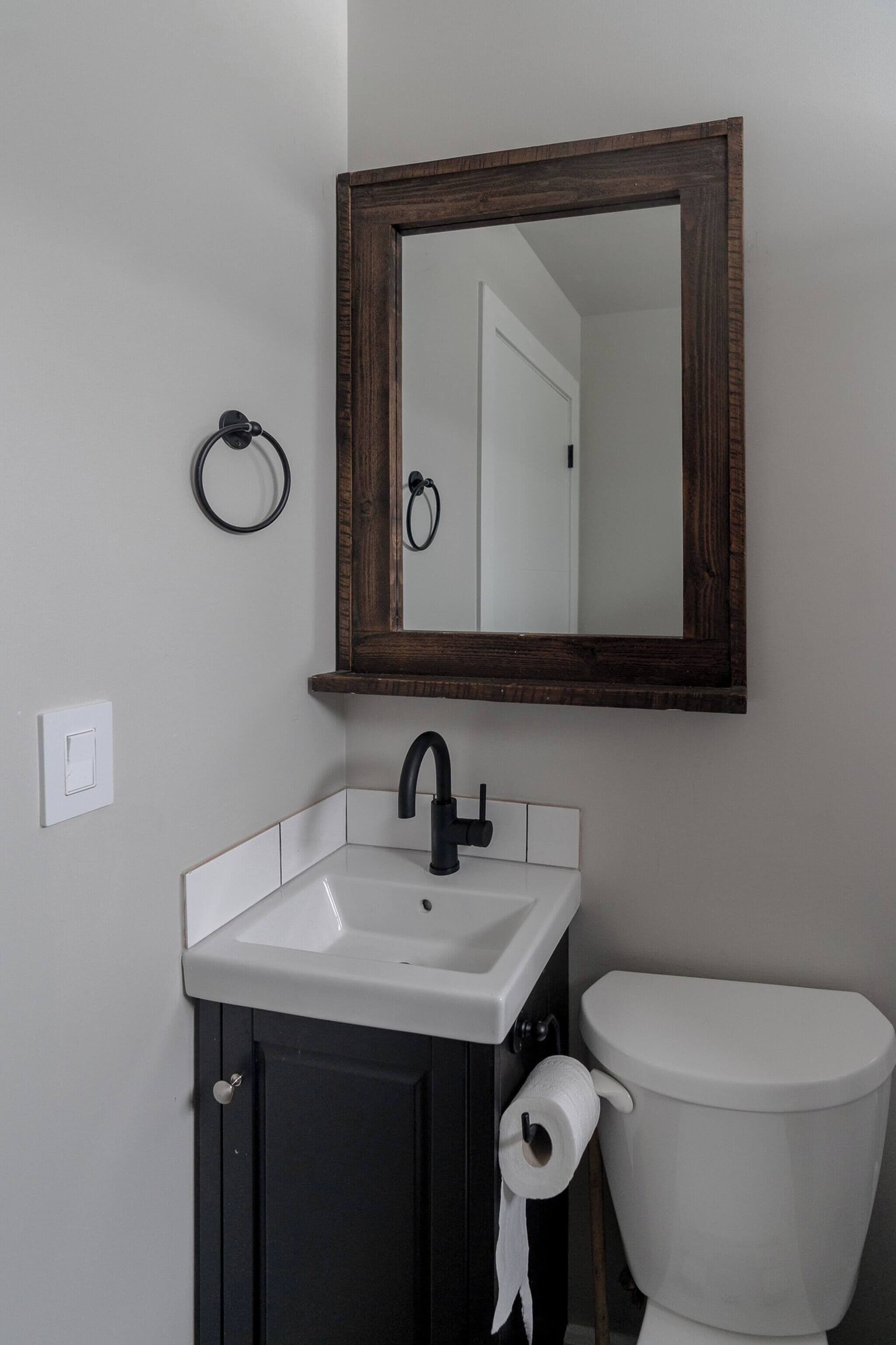 A bathroom with a white sink, dark cabinet, and a white toilet.