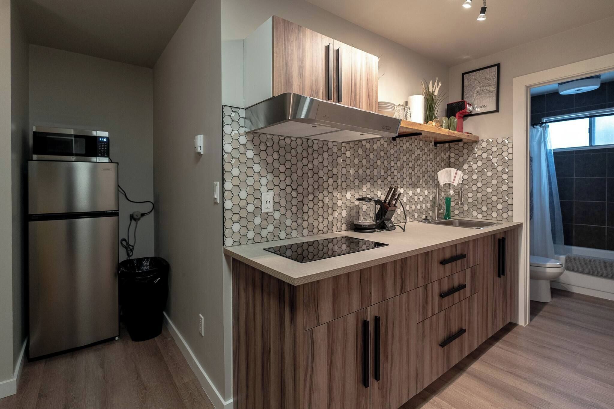 A modern kitchen with a stainless steel refrigerator, wooden cabinets, a hexagonal tile backsplash, and a window with a curtain.