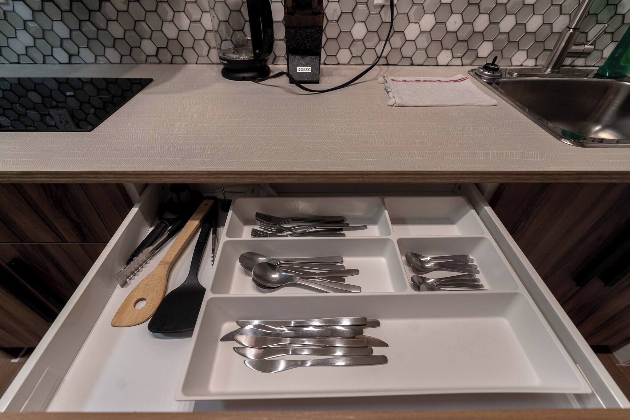 Cozinha com bancada branca, pia e gaveta com utensílios.