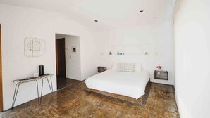 Ein Schlafzimmer mit einem großen Bett, einem Nachttisch, einer Wandablage und einer Tür zu einem anderen Raum.