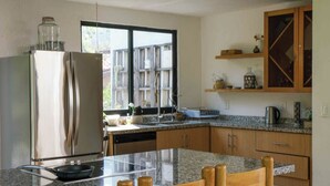 Eine moderne Küche mit Edelstahlkühlschrank, Holzhocker, Granitarbeitsplatten und Pendelleuchten.