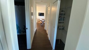 Un pasillo estrecho con piso de madera, paredes blancas y una puerta que da a una habitación con cama y televisor.