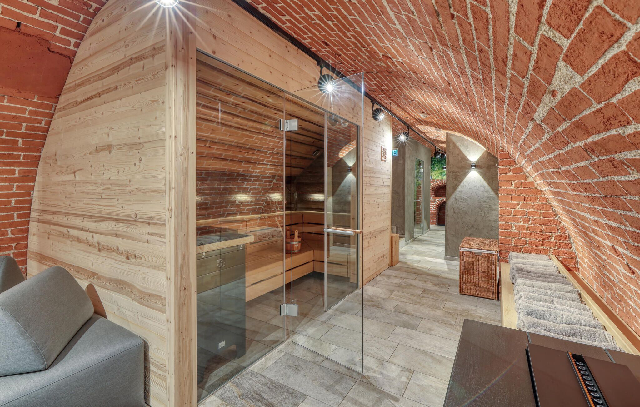 A sauna room with wooden walls, glass doors, and a brick archway.