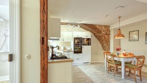 A kitchen with white cabinets, a brick arch, a dining area with wooden chairs, and a hanging pendant light.