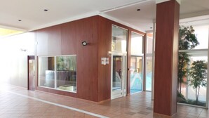 Un vestíbulo amplio con suelo de baldosas, paneles de madera y grandes puertas de cristal que dan a otra zona.