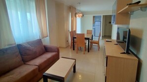 Una sala de estar con un sofá, una mesa de centro, un televisor y un comedor con sillas y una mesa.