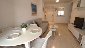 A modern living space with a dining area, a sofa, a TV, and a small table with a plant. - ACV - Acapulco IV-1st floor line 4 South (OROPESA)