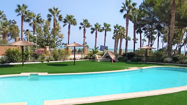 A swimming pool with artificial grass, surrounded by palm trees and a fence. - ACV - Acapulco IV-1st floor line 4 South (OROPESA)