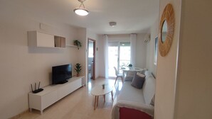 A modern living room with a flat-screen TV, a white sofa, a small dining table, and a white cabinet. - ACV - Acapulco IV-1st floor line 4 South (OROPESA)