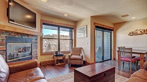 Una sala de estar con sofás de cuero, chimenea, televisor de pantalla plana y comedor con sillas.