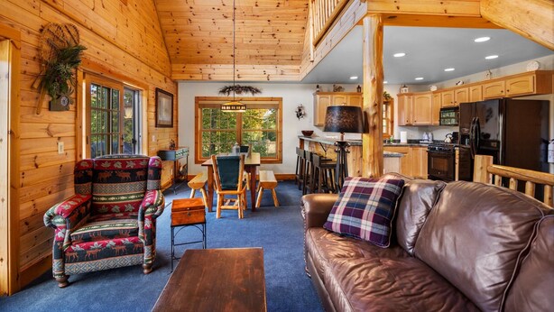 A log cabin interior with a wooden dining area, a sofa, and a kitchen with wooden cabinets and appliances. - Ski & Golf Spacious Log Cabin in Otsego Resort (Gaylord)
