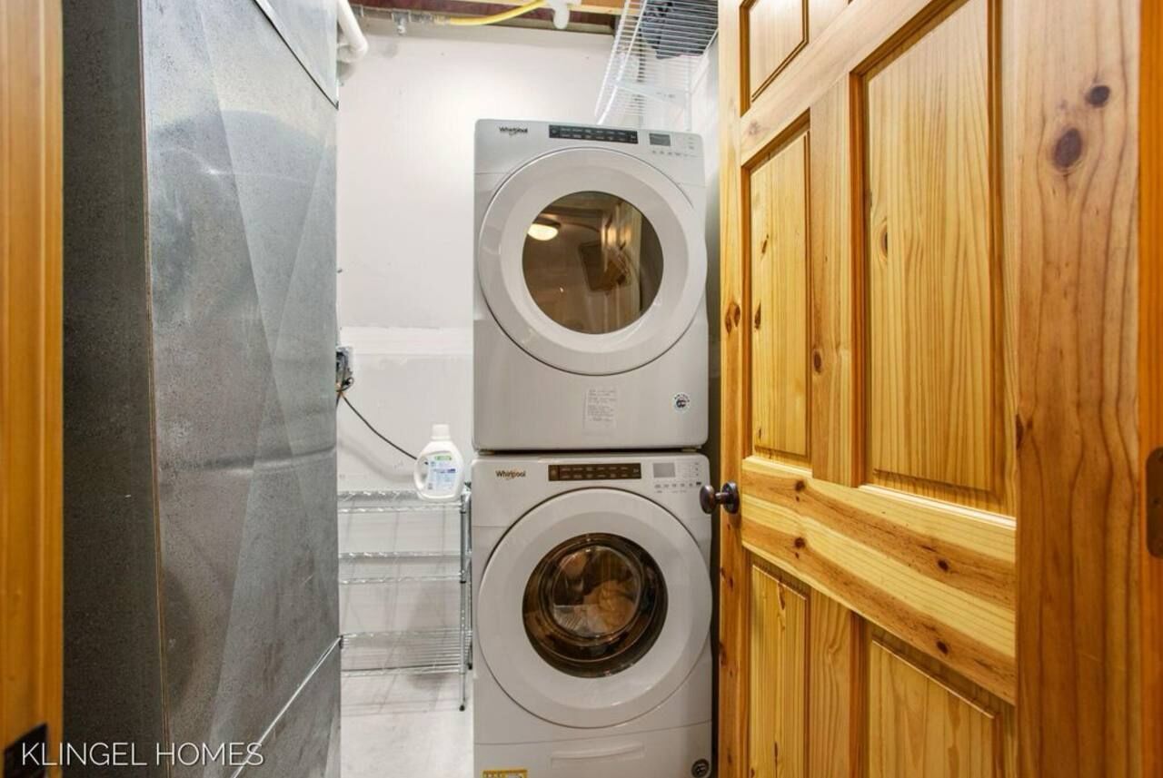 Un lavadero con dos lavadoras y secadoras Whirlpool apiladas, armarios de madera y una botella de agua en un estante.