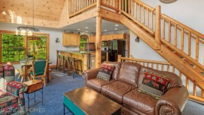 A spacious living area with a wooden staircase, a leather sofa, and a dining table. - Ski & Golf Spacious Log Cabin in Otsego Resort (Gaylord)
