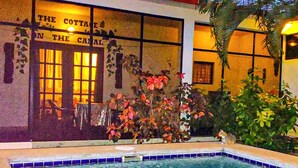 A pool area with clear water, a sign reading "The Cottage on the Canal", and surrounding greenery. - 1 Bedroom Canal Cottage, Pool, Fishing, BTB Approved, Quiet, Bikes, Kit, Laundry (Corozal Town)