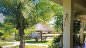 A hammock under a palm tree, a thatched-roof structure, and a pathway with white pebbles. - 1 Bedroom Canal Cottage, Pool, Fishing, BTB Approved, Quiet, Bikes, Kit, Laundry (Corozal Town)