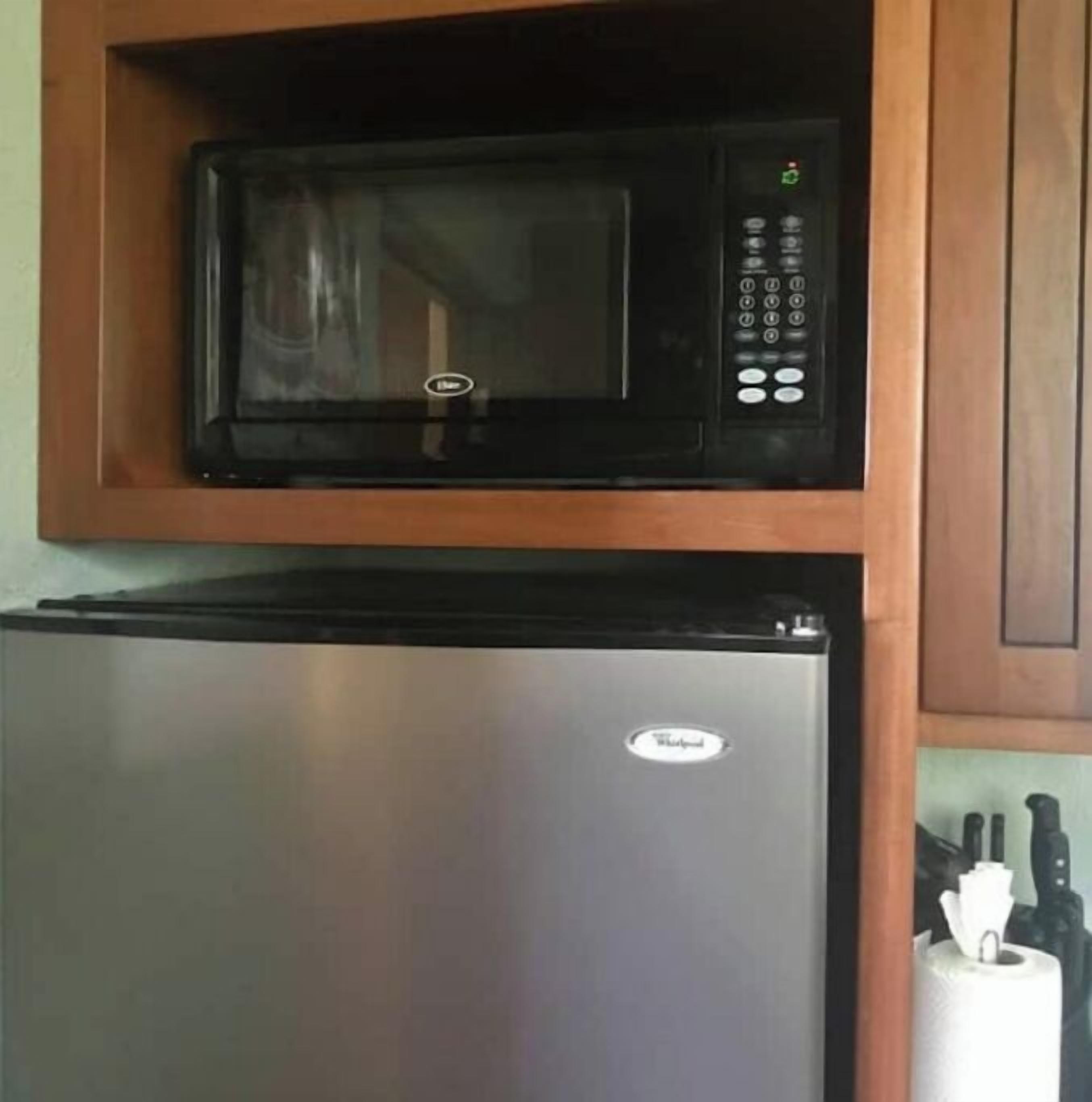 A compact kitchen with a black microwave and a stainless steel refrigerator.
