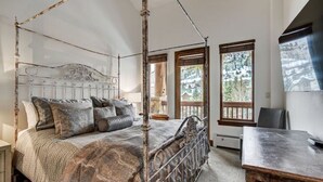 A four-poster bed with a wooden frame and a patterned bedspread, a wooden desk, and a large window with a view of trees. - Ski-in/Ski-out | Spacious 1BR+Loft for 4 (Avon)