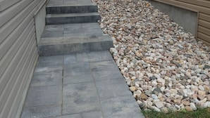 A pathway between two buildings with a stone-tiled floor and a gravel bed on one side.