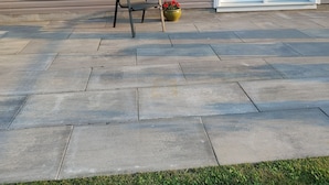 A patio with a chair and a flower pot, a house with large windows, and a door.