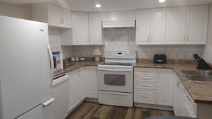 A kitchen with white cabinets, a stove, a refrigerator, and a microwave.