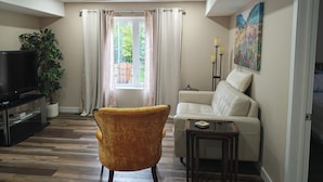 A living room with a sofa, armchair, TV, and a painting on the wall.