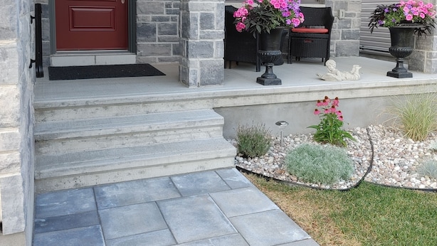 A stone house with a red door, a covered porch, and a small garden with pink flowers.
