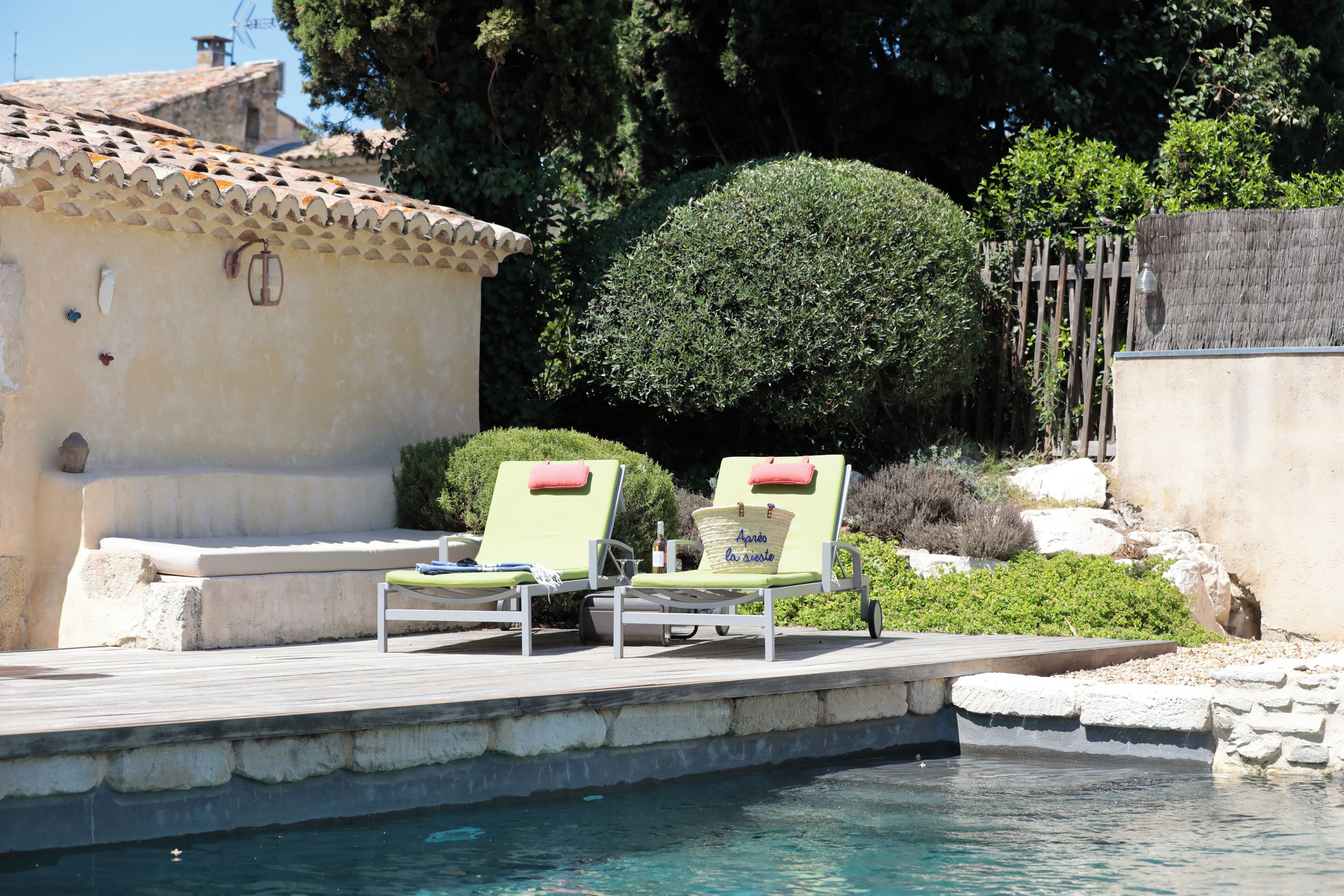 A poolside area with two lounge chairs, a stone wall, and a neatly trimmed bush.