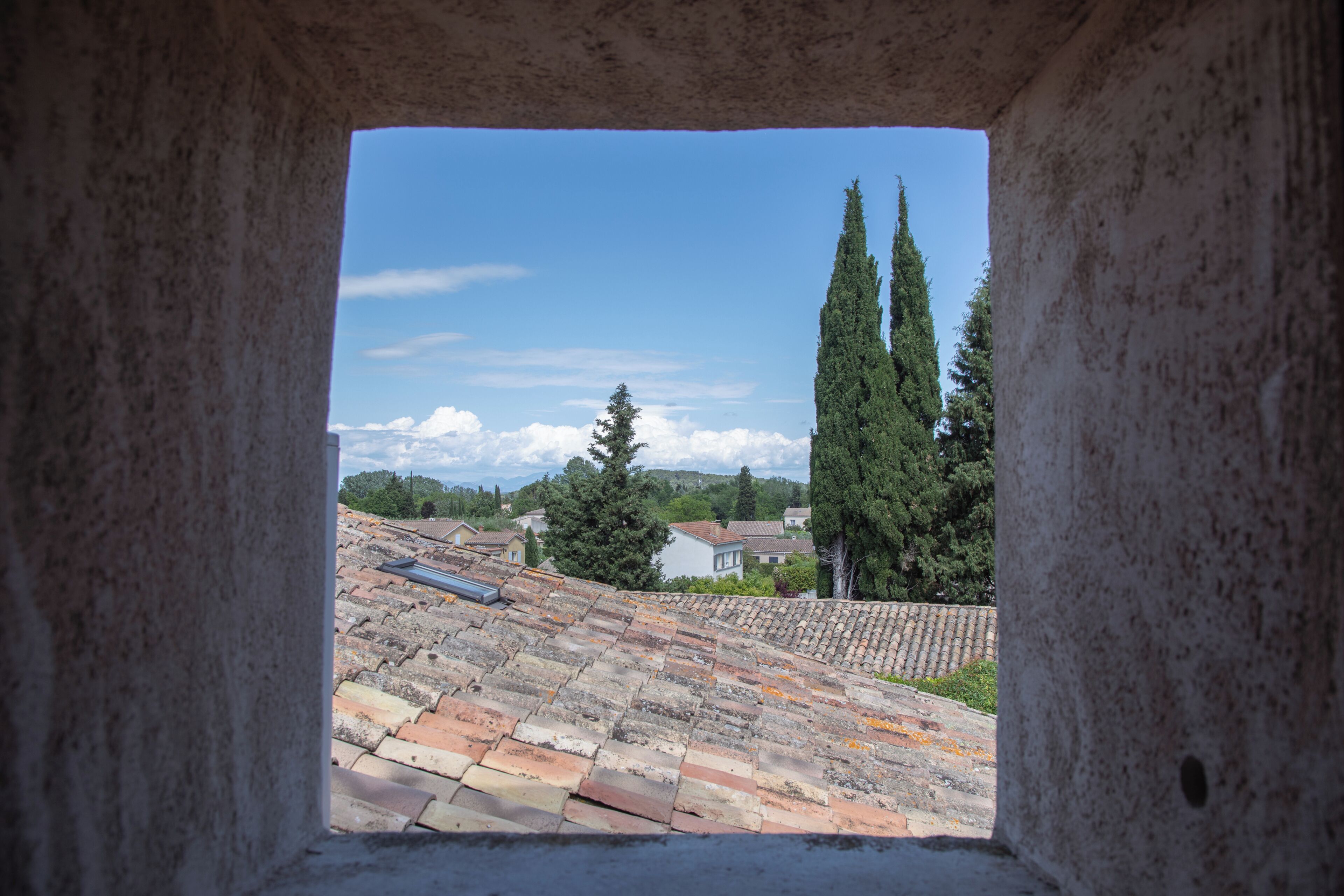 A stone structure with a view of a tiled roof, trees, and houses in the distance.
