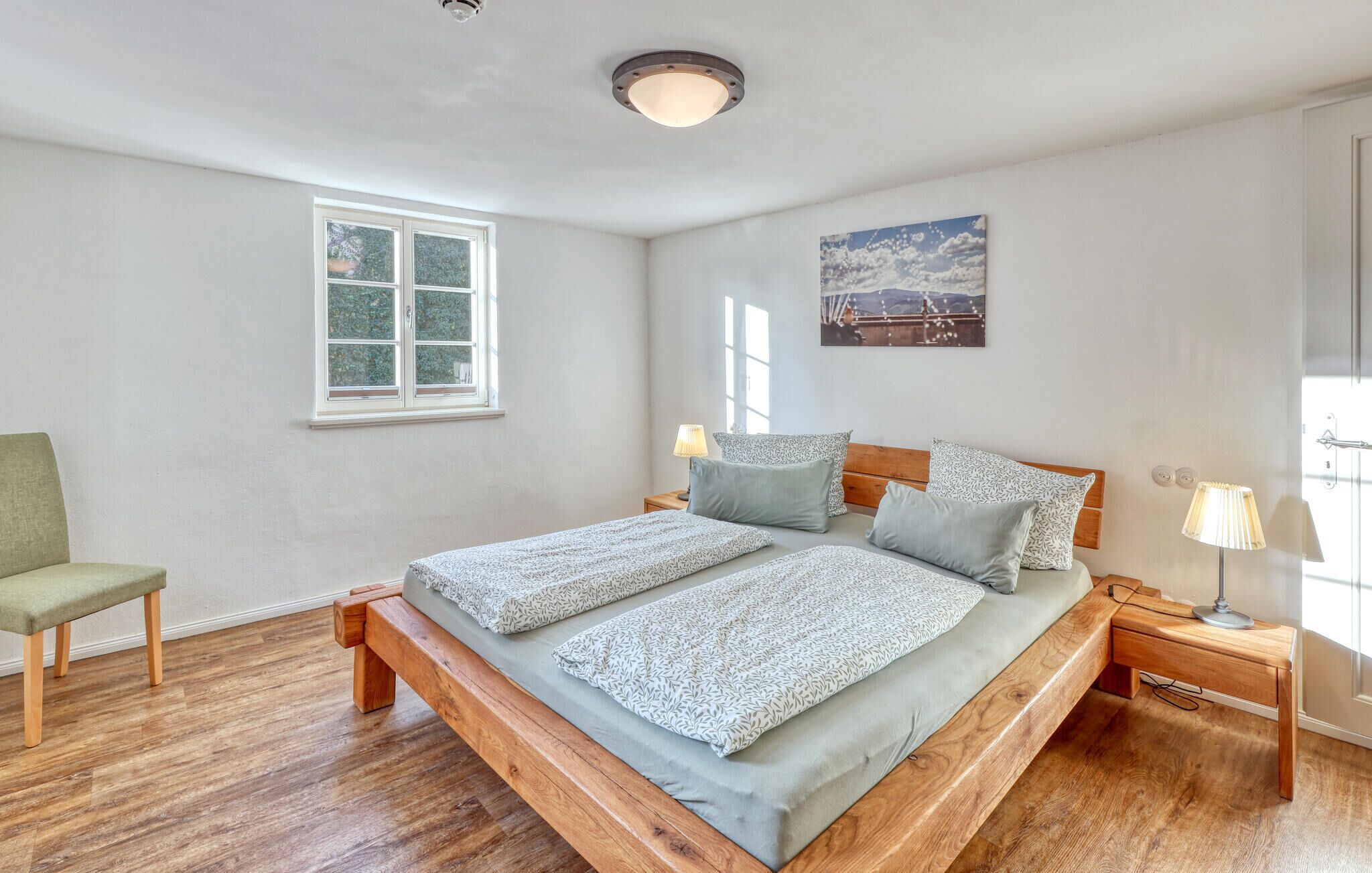 A bedroom with a wooden bed, two bedside tables, a chair, and a window.