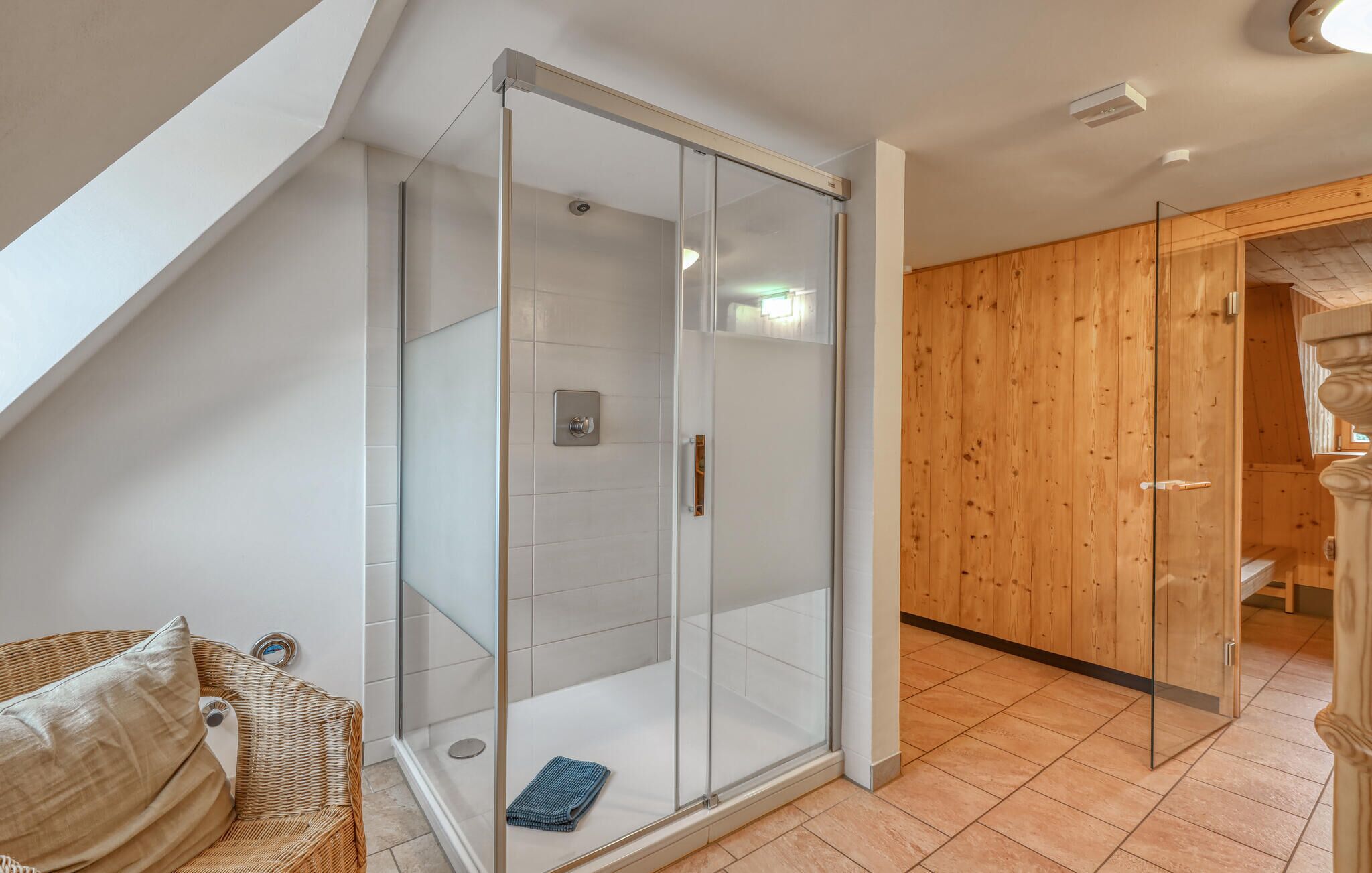 Un baño moderno con cabina de ducha de vidrio, una puerta de madera y una silla de mimbre con cojín.