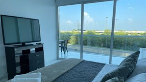 A modern bedroom with a large bed, a flat-screen TV on a black dresser, and a balcony with a view of the road and greenery. - Apartamento en Cartagena de Indias, Edificio Morros 3 (Cartagena)