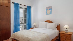 A bedroom with a bed, two bedside tables with lamps, a wooden wardrobe, and a window with blue curtains.