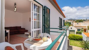 A balcony with a table, chairs, a sofa, and a view of the surrounding neighborhood.