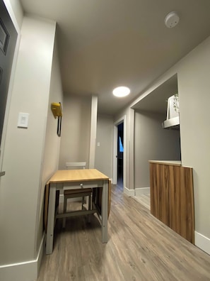 A hallway with a wooden table and bench, a white wall, a ceiling light, and a door leading to another room. - Brand New Modern Flat 2br1ba Whyte And U (Edmonton)