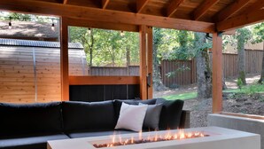 A covered outdoor seating area with a white fire pit and a black sofa with cushions. - Eugene Evergreen Escape by Les Chalets Stays is a fully renovated home perfect for your crew! Game room, play house, sauna, outdoor entertaining space and huge back yard. (Eugene)