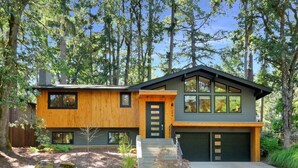 A modern two-story house with a combination of wooden and grey siding, a front entrance with a glass door, and a driveway leading to a garage. - Eugene Evergreen Escape by Les Chalets Stays is a fully renovated home perfect for your crew! Game room, play house, sauna, outdoor entertaining space and huge back yard. (Eugene)